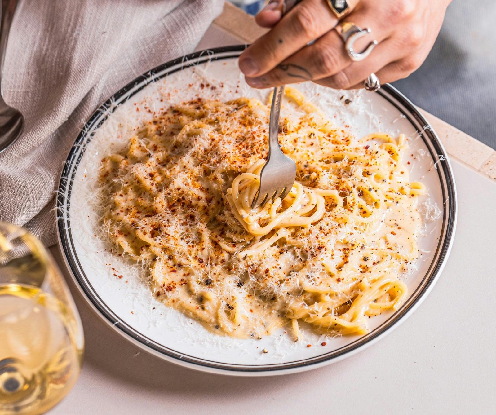 A plate of cacio e pepe sprinkled with cheese and red aleppo pepper