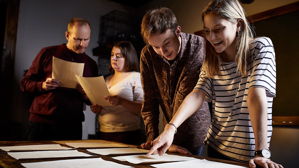 4 people pointing at clues on a table and smiling
