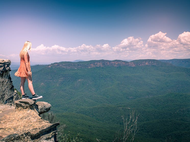 Girl standing on rock cliff edge overlooking valley