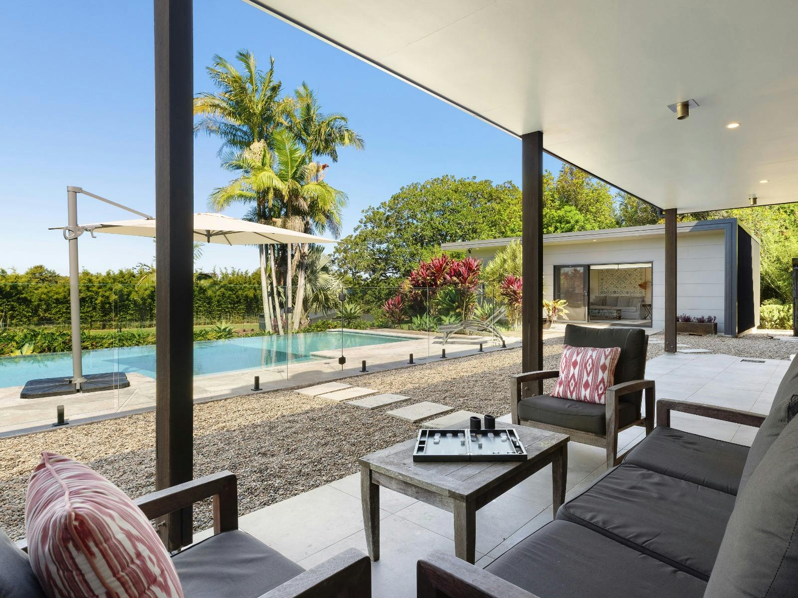 Covered outdoor lounge with views across the pool, gardens and guest pavilion.