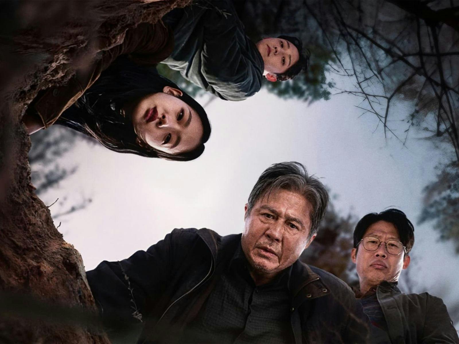 Three men and one woman covered in dirt all peering down into a ditch