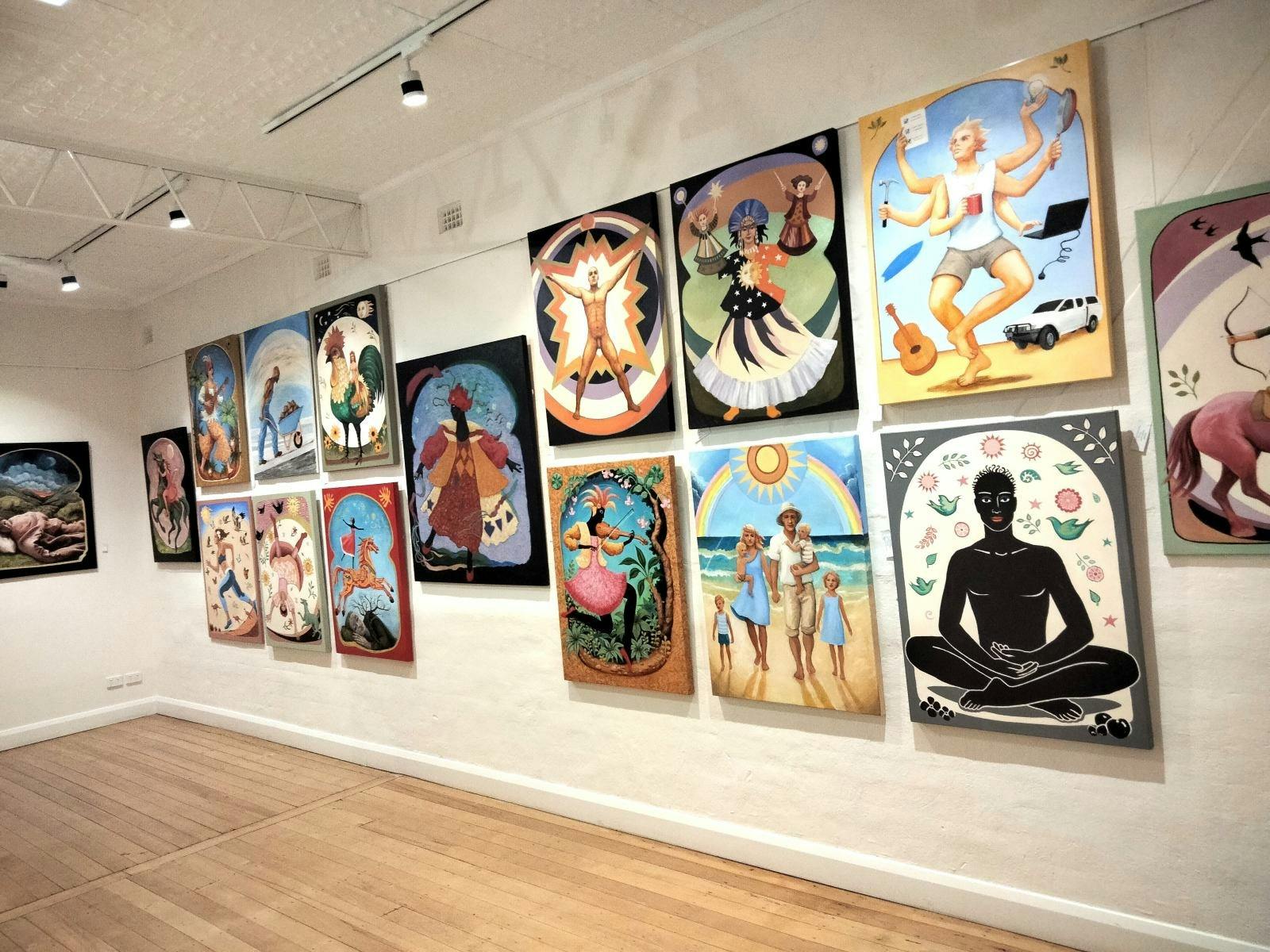 Lots of large colourful paintings on a big white wall.