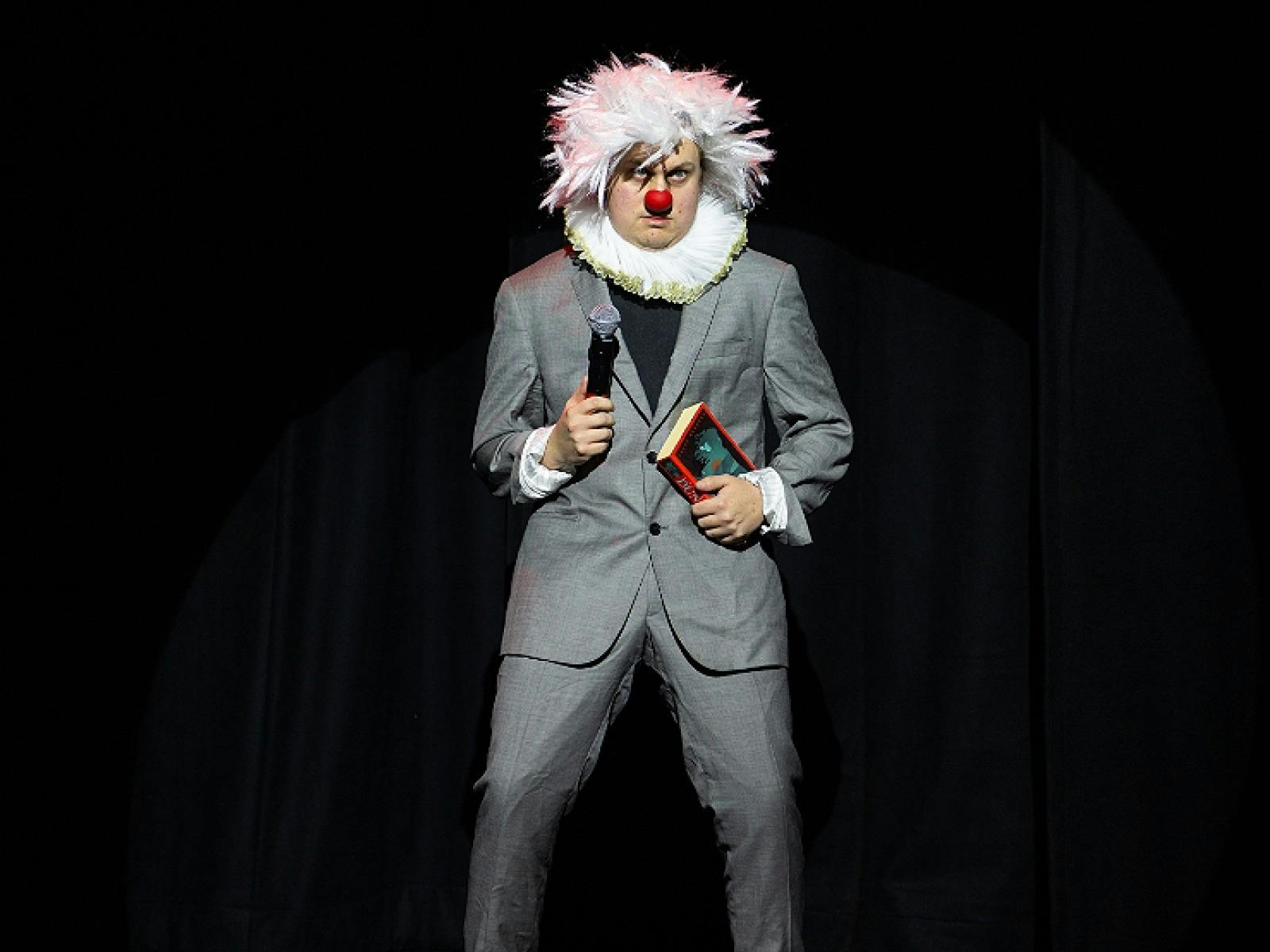 Artist in grey suit with white afro wig , red nose and white frilly color
