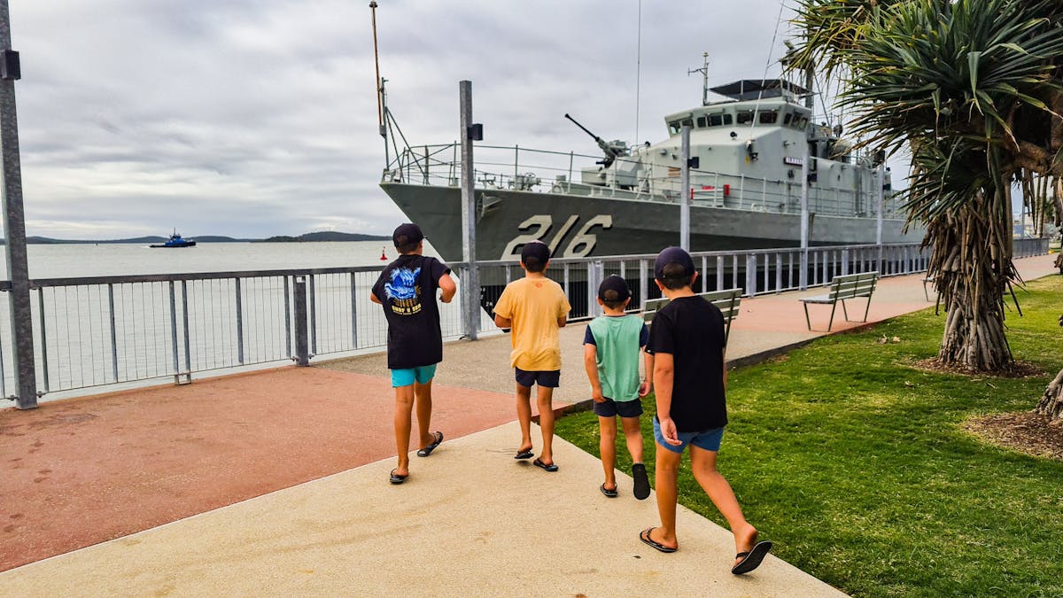 4 boys walking along a walkway with the HMAS Gladtsone in background 4 boys walking along a walkway with the HMAS Gladtsone in background