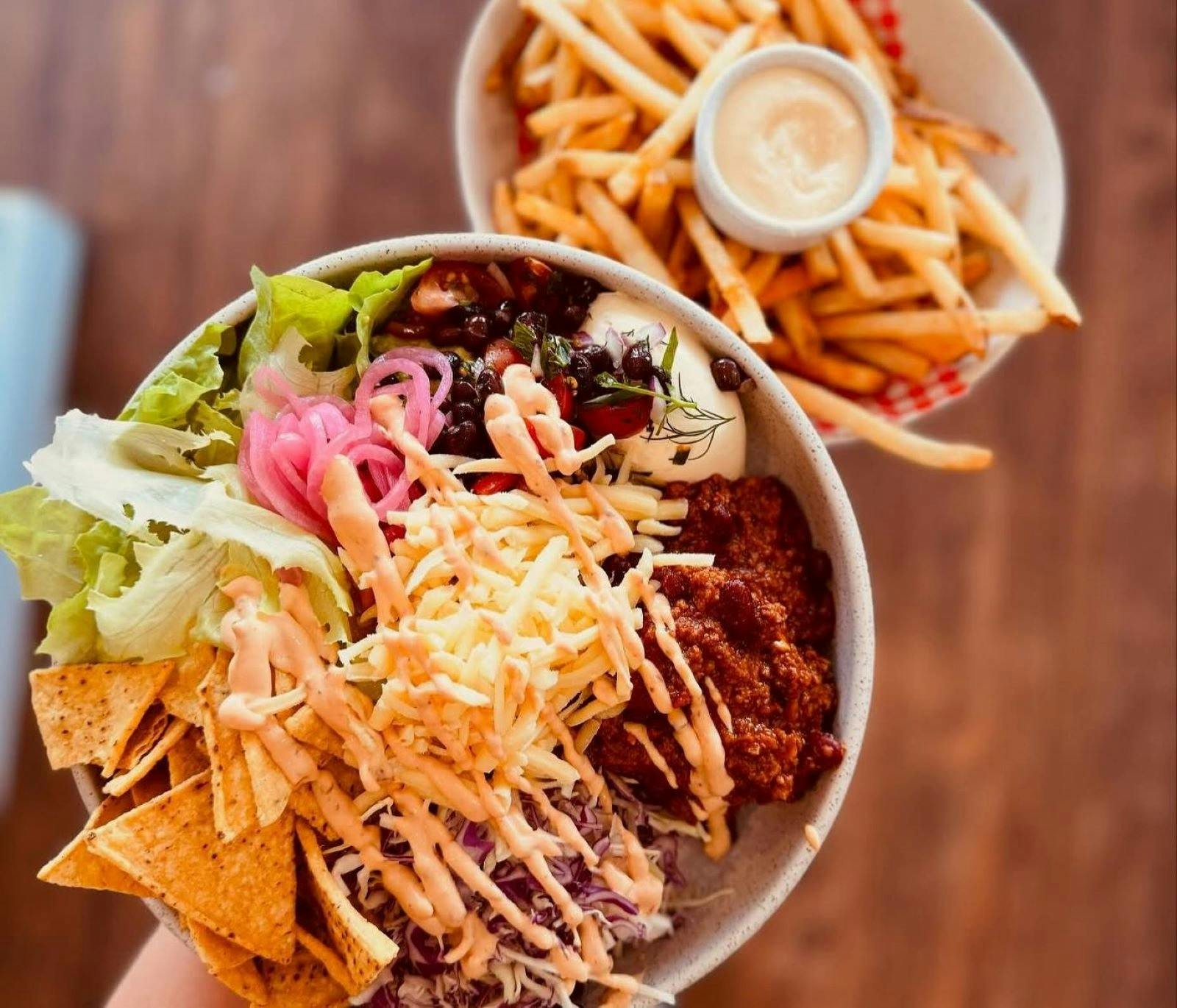 A full bowl of special nachos, salad and more with chips and dip in the background