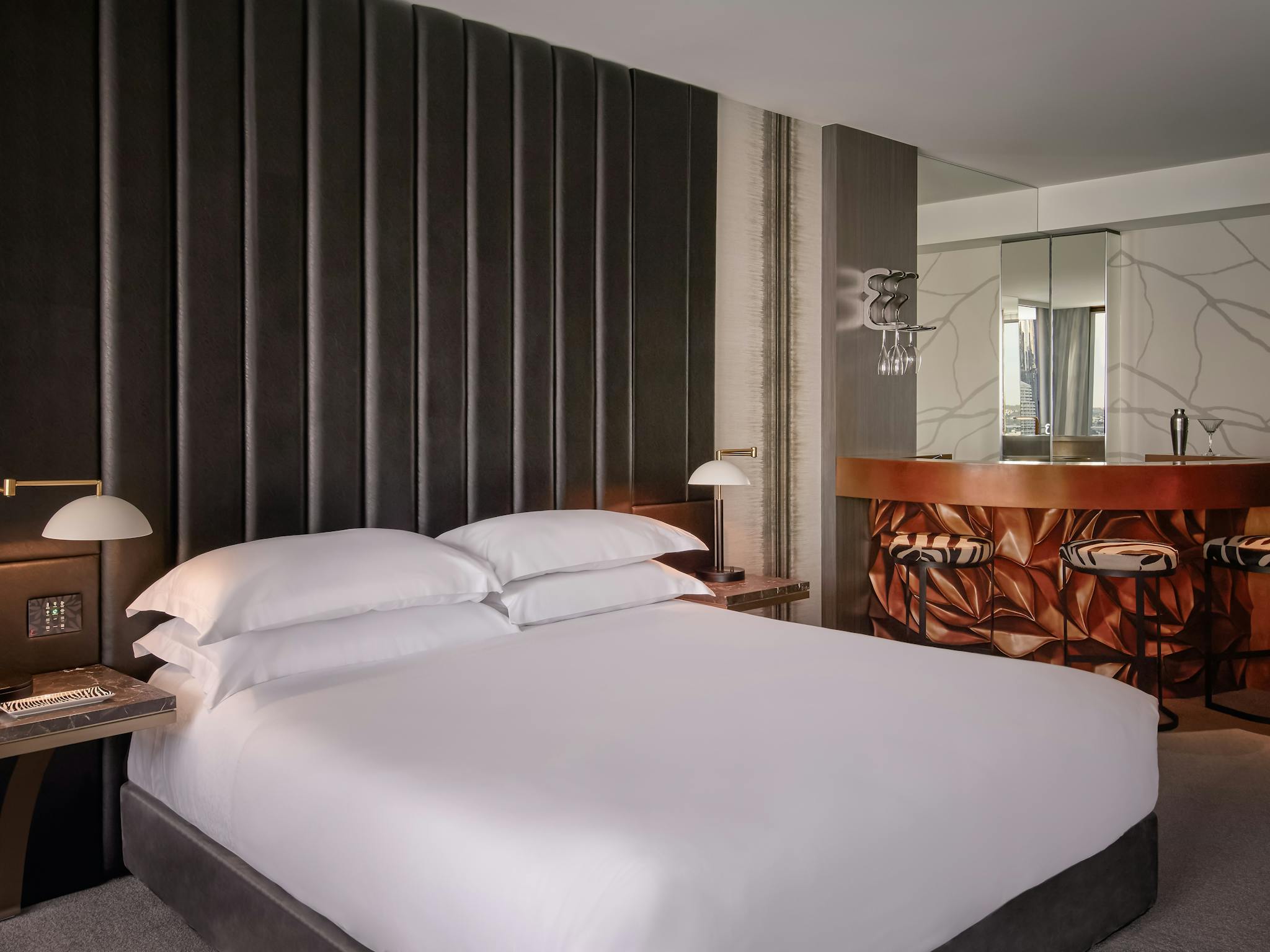 Luxury hotel suite with a king bed, sculpted bar area and warm lighting throughout the space Luxury hotel suite with a king bed, sculpted bar area and warm lighting throughout the space