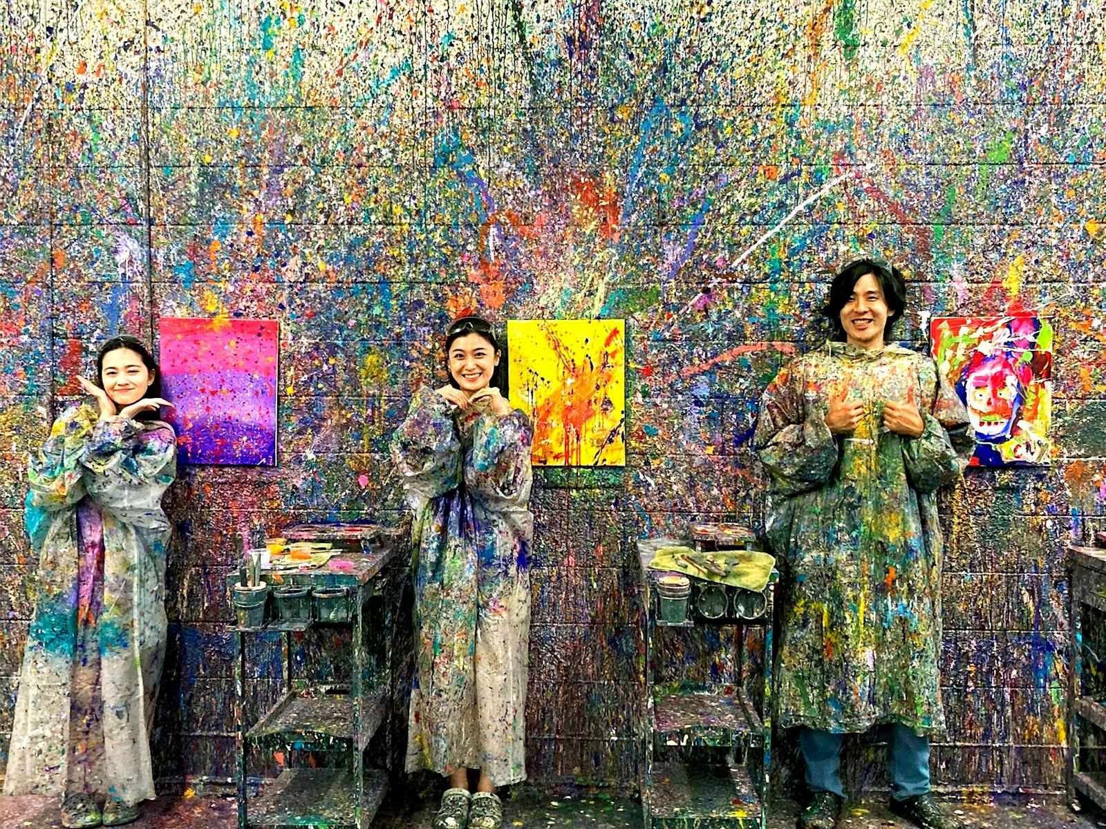 Friends displaying splatter paint artwork in front of colourful wall, Kaboo Studio