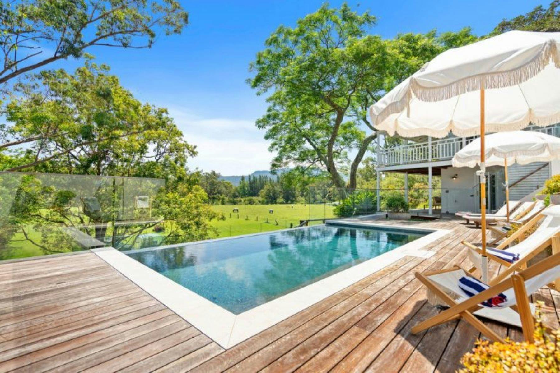 Image of pool. Backdrop of farmland and trees. Umbrella sits above pool area.