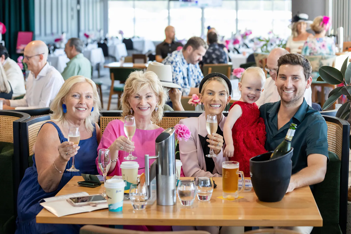 Family of four and a little girl in a red dress holding up their drinks and smiling at the camera