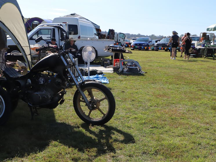 Front wheel and tank of a motorcycle in foreground, grassy area and caravan behind