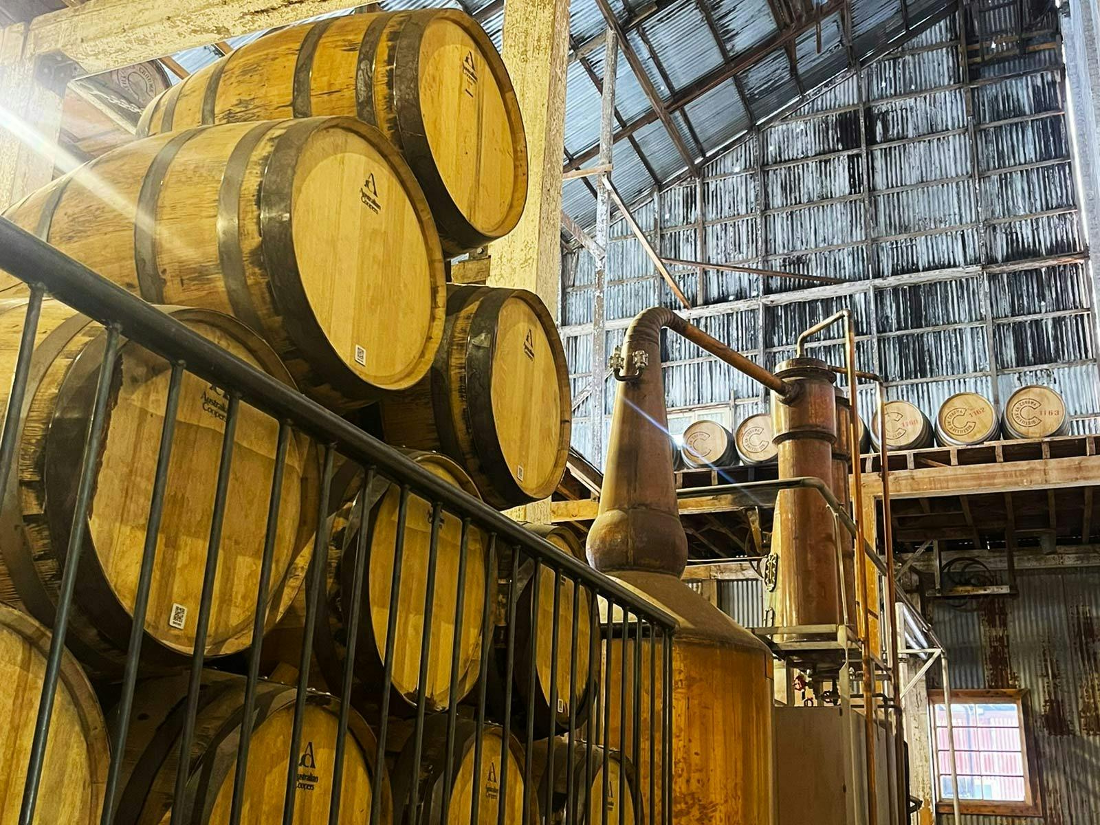 Wine barrels next to a still in an old building in Corowa