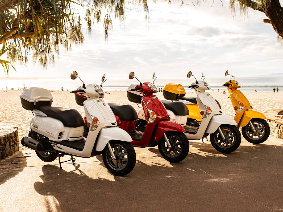 Line up of 4 different scooters at Noosa Main Beach at sunset