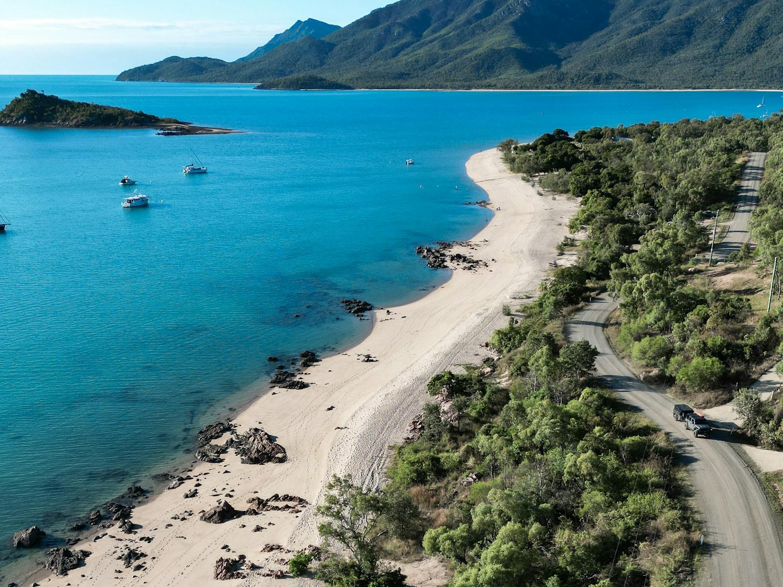 Aerial view of Hydeaway Bay with a sandy beach, coastal road and boats on the blue calm waters