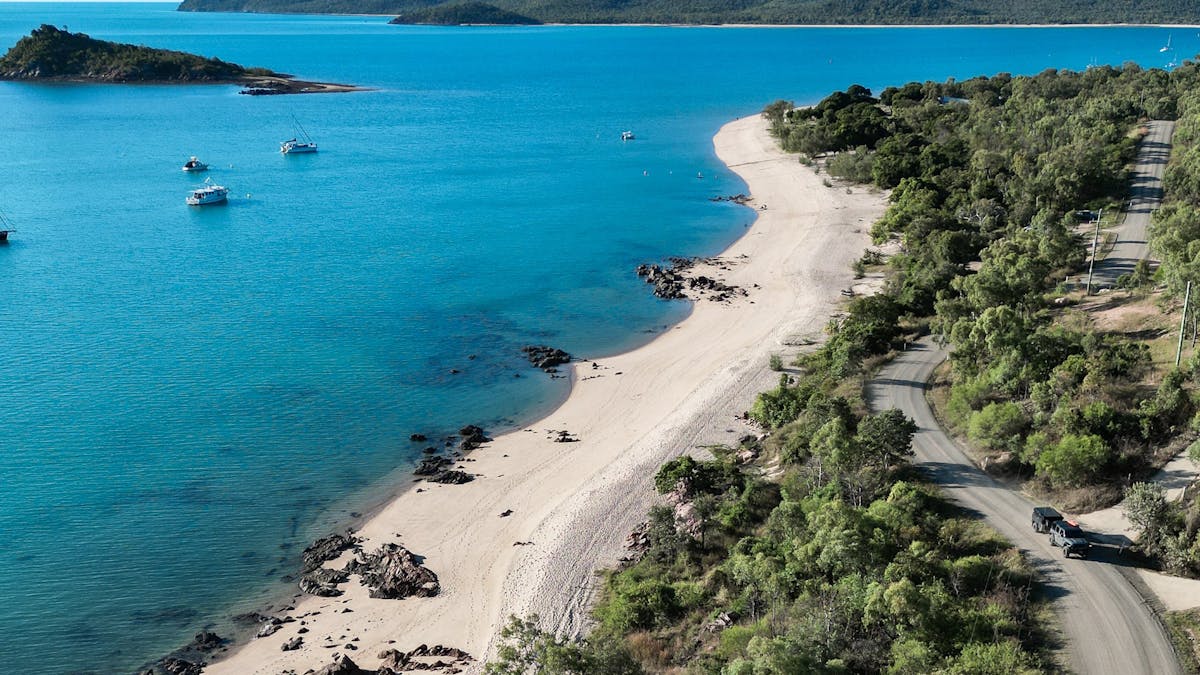 Aerial view of Hydeaway Bay with a sandy beach, coastal road and boats on the blue calm waters