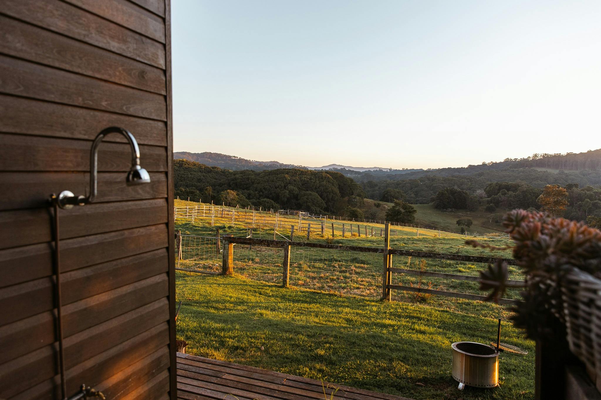 A green farm is in the distance with a shower head attached to a timber wall