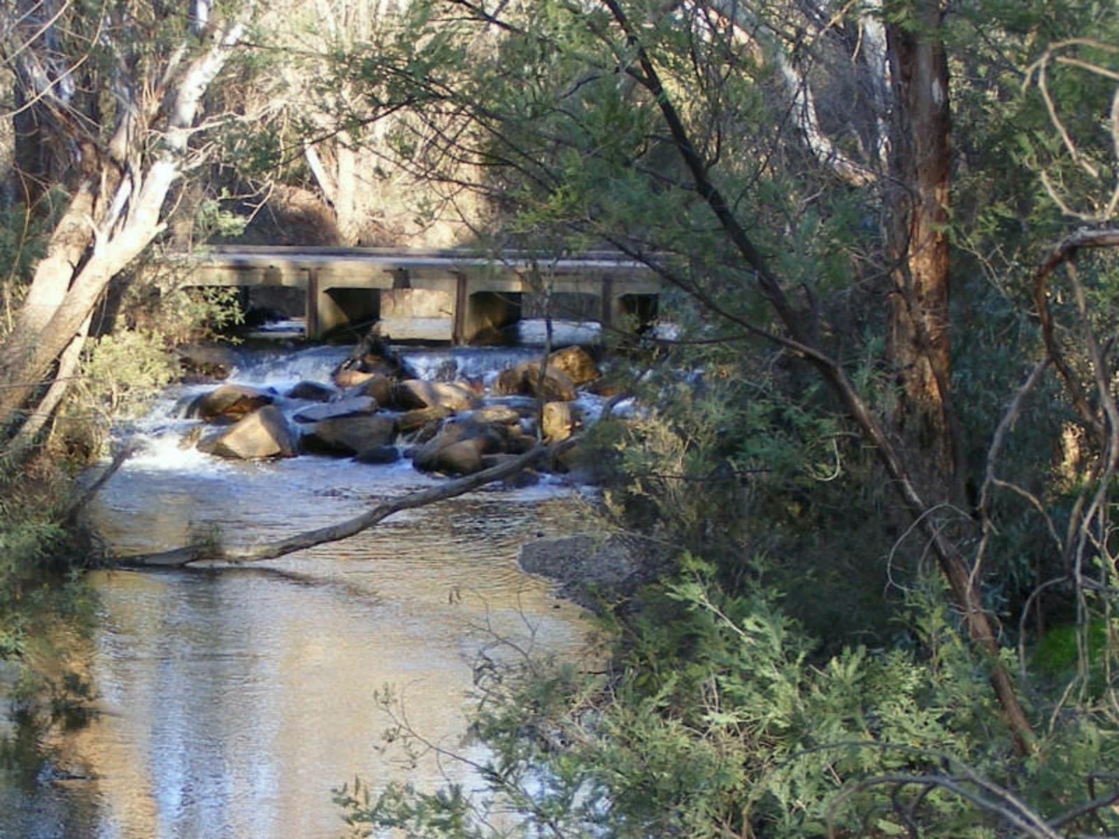 Bridge, water flowing underneath through rocks, trees, sunny day.