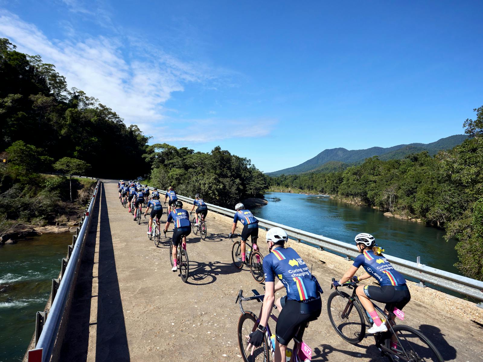 Cycle peloton crossing bridge in formation taken from behind cyclists, scenic