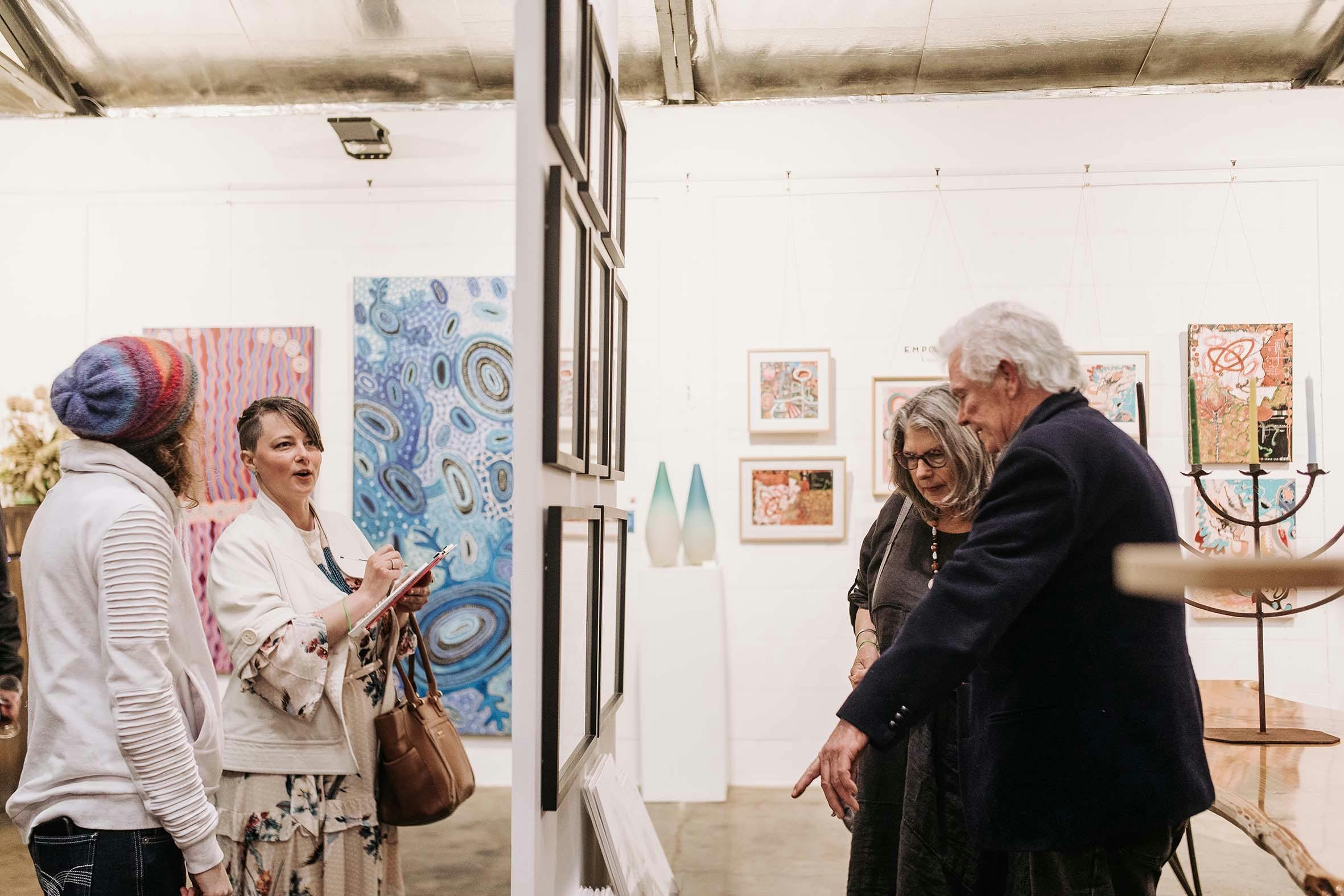 4 people looking at either side of a hanging panel in an exhibition of art woks on a wall