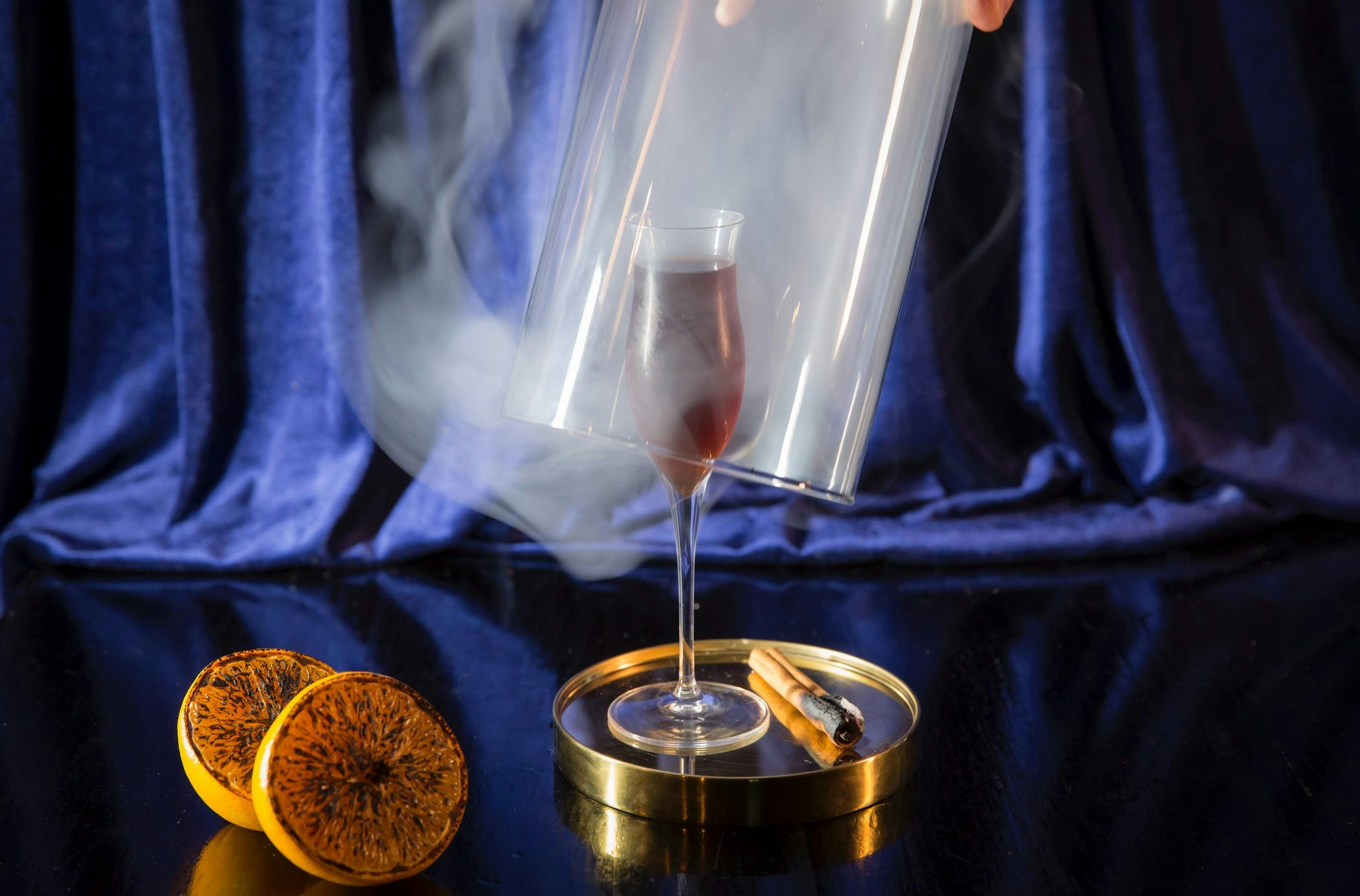 A cloche being lifted over a smoke filled glass with a cinannamon stick