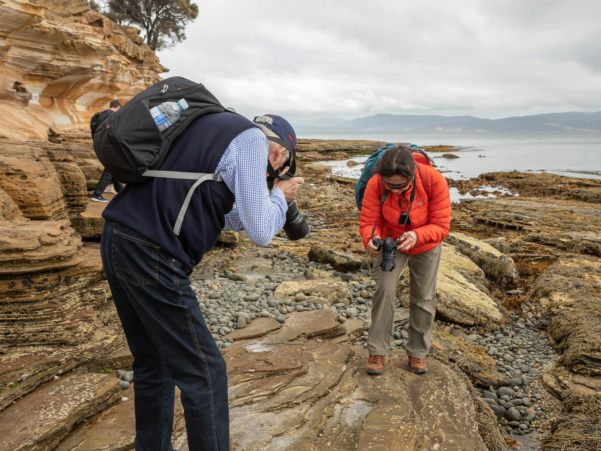two photographers on a rocky foreshore looking at the rocky grounding taking photos