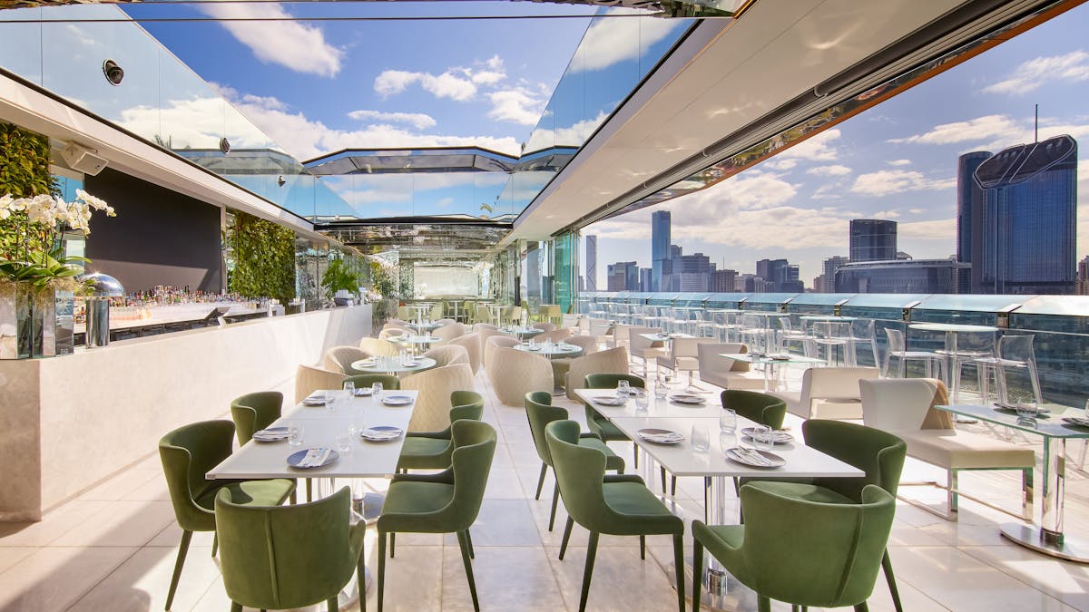 Rooftop bar with open-air dining, green chairs and skyline views on a sunny day
