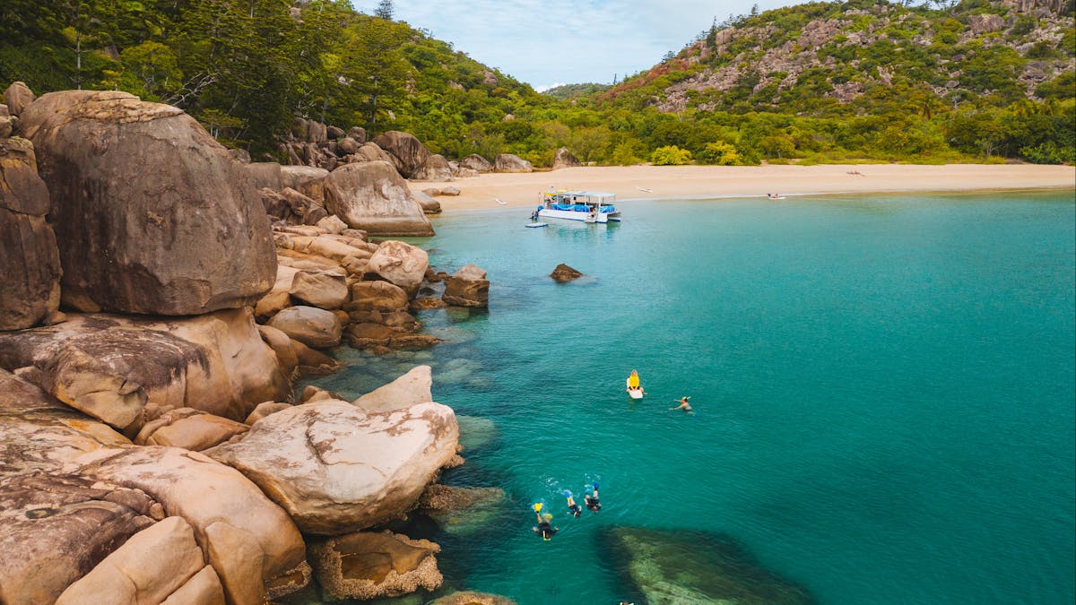 rugged beautiful rocky coastline with boat near the beach and people snorkelling near beach, sunny