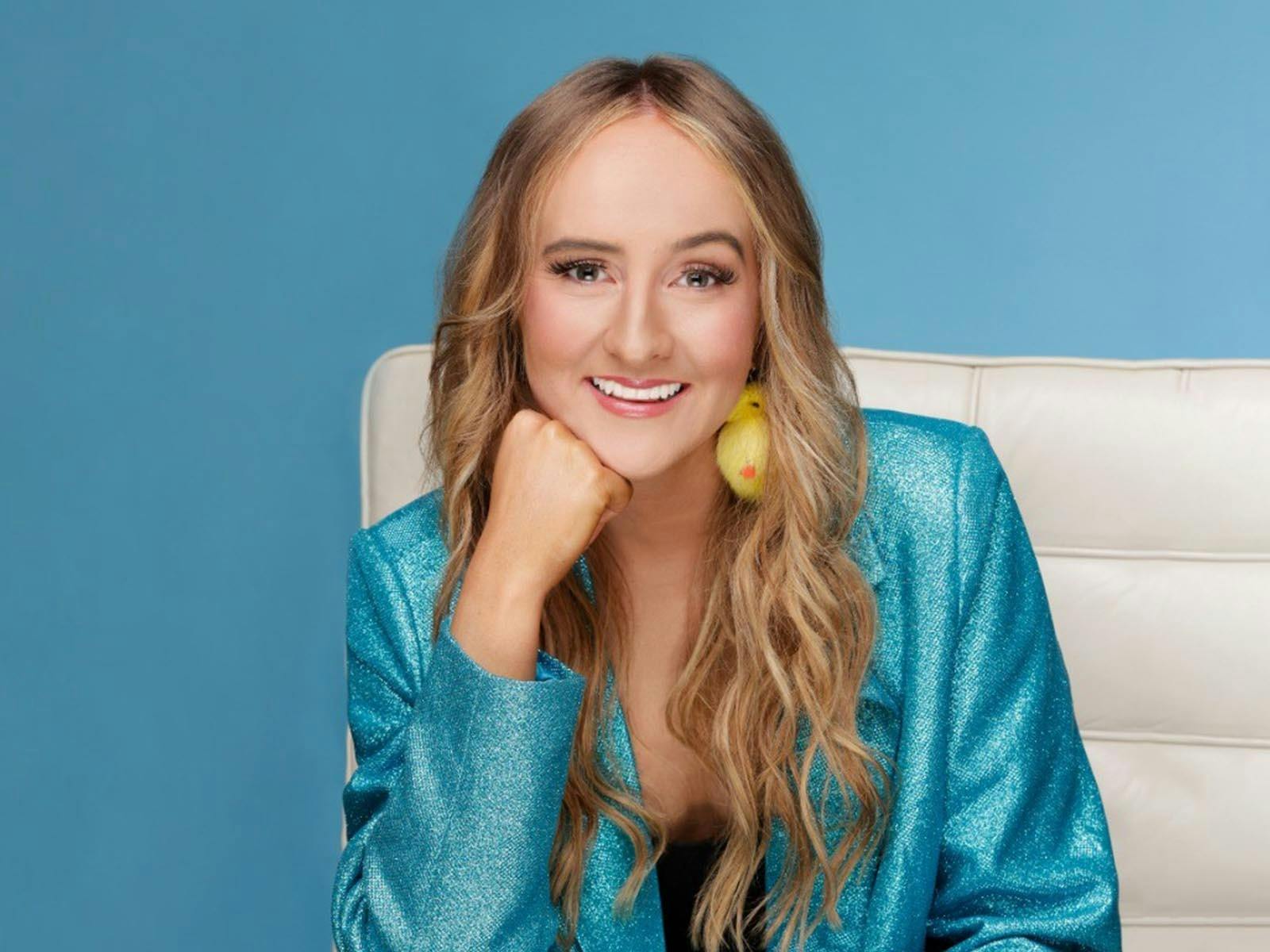 A white woman with long blonde hair smiling at the camera, wearing a light blue blazer