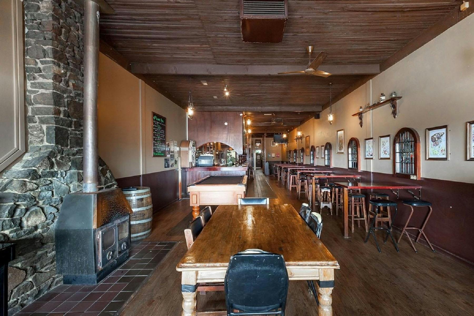 Pot belly woodfire on left-hand wall surrounded by stonework, with seating area and pool table throu