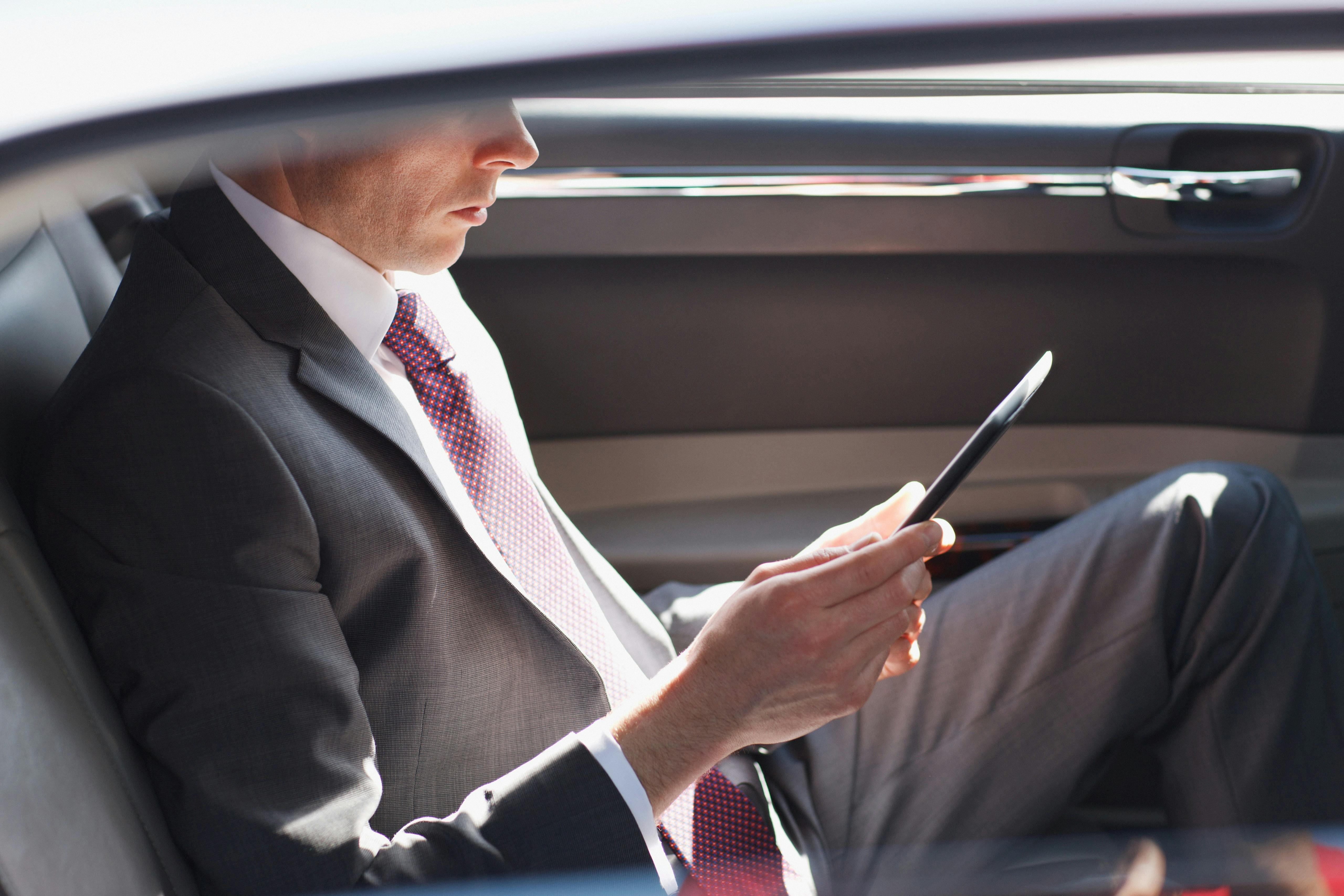 A business man sitting in the back of a car doing their work