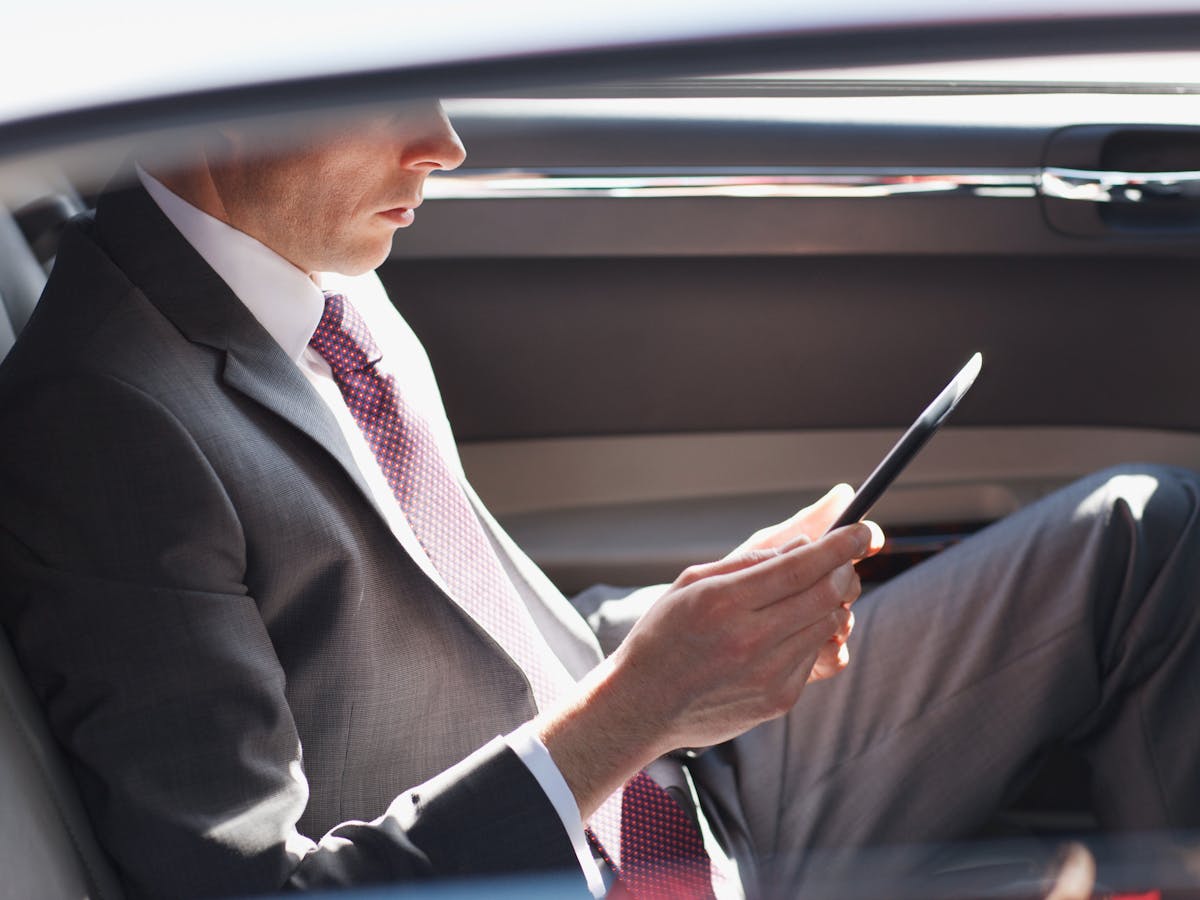 A business man sitting in the back of a car doing their work