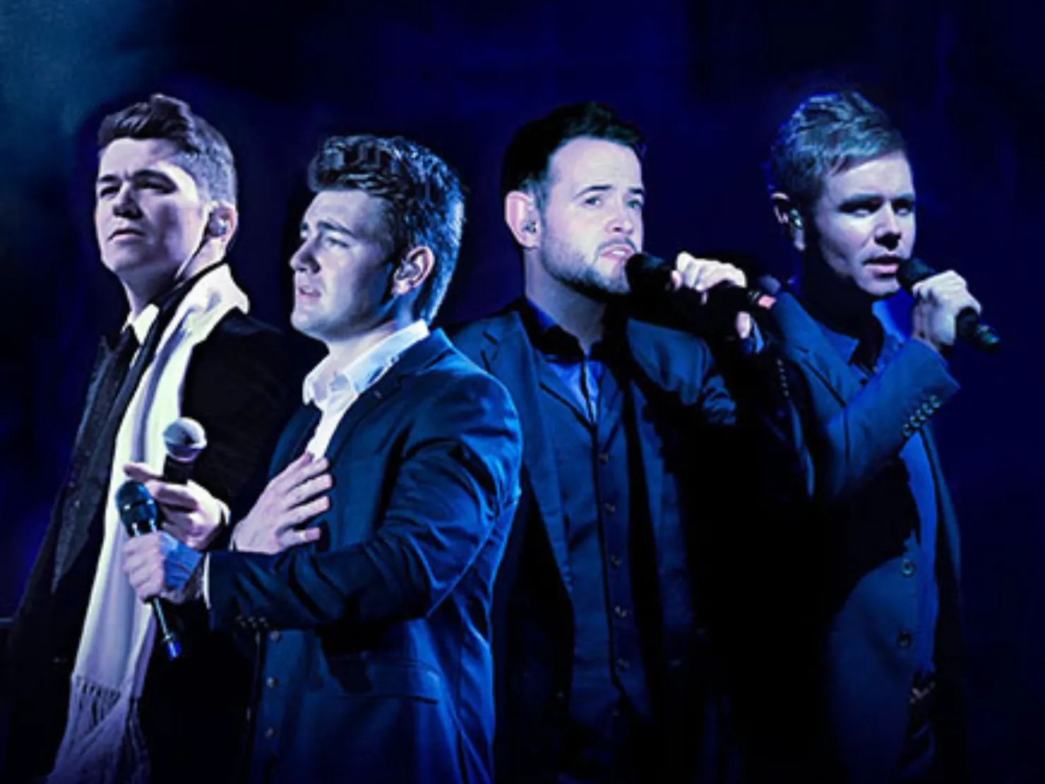 4 men in blue suits with microphones up to their mouths
