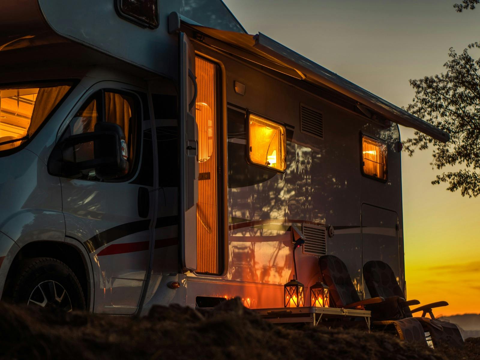 Ein weißes Wohnmobil wird vom Schein der untergehenden Sonne und von Kerzenlampen beleuchtet.
