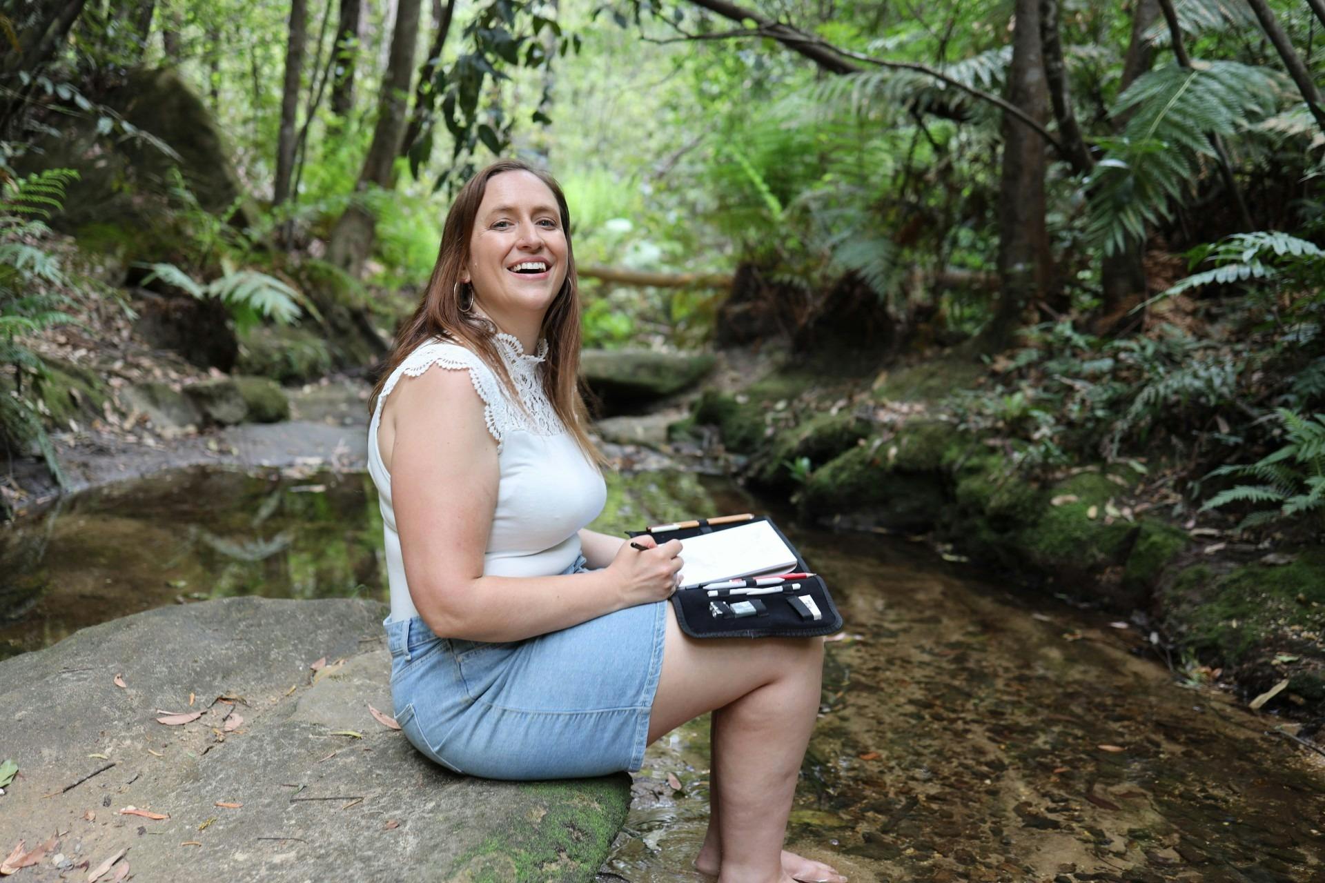 Lady doing charcoal drawing mindfulness session at creek