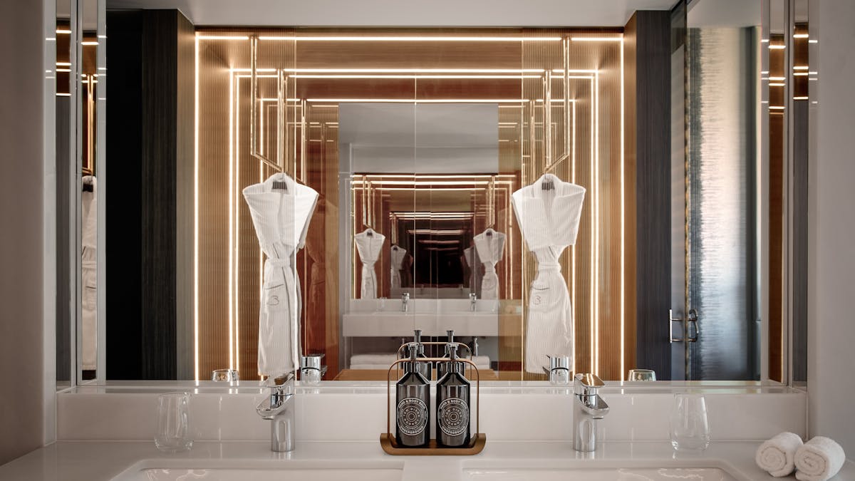 Luxury double vanity with robes and warm backlit mirrors reflected in glass
