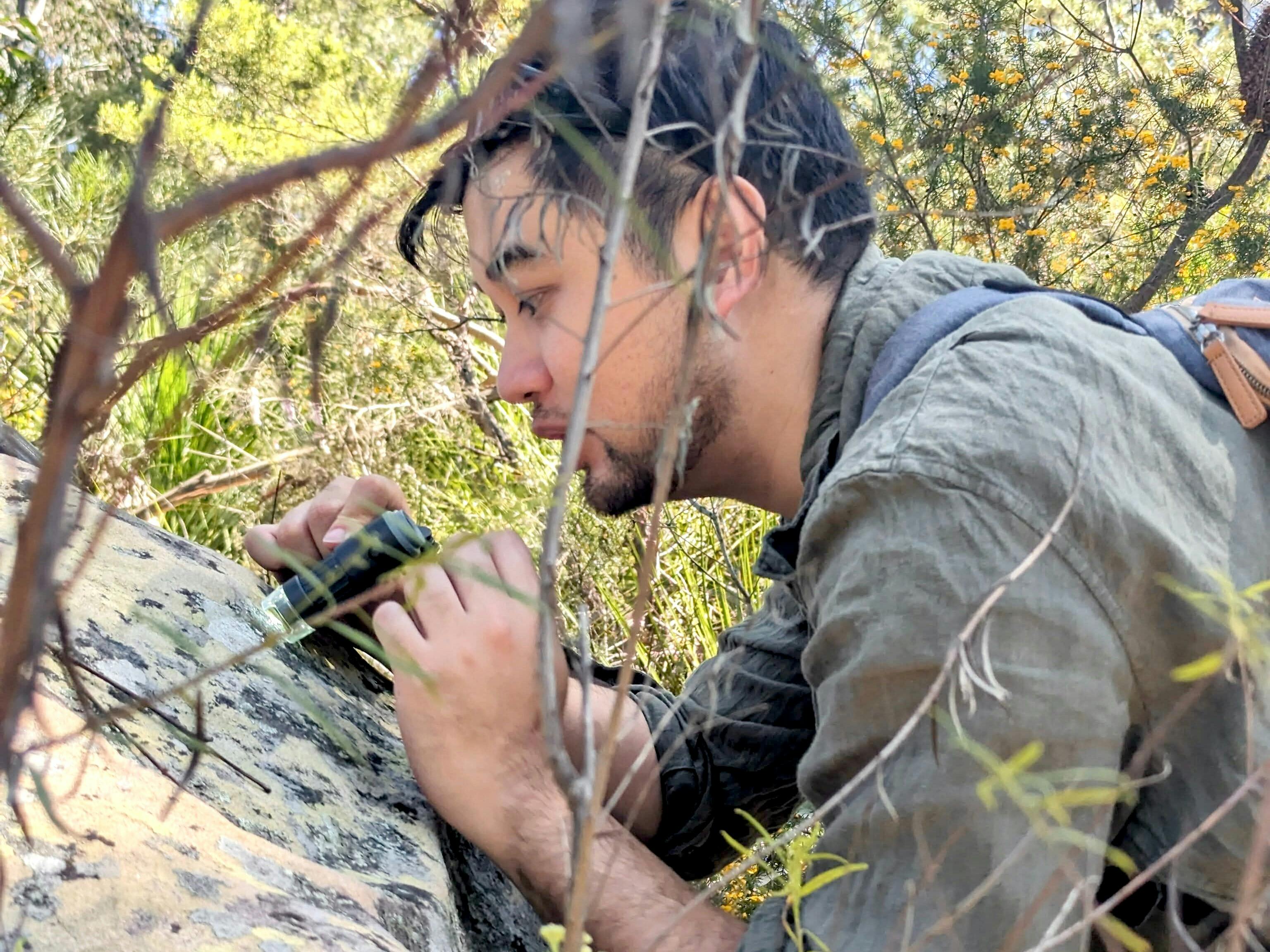 A man looks down the lens of a hand held microscope