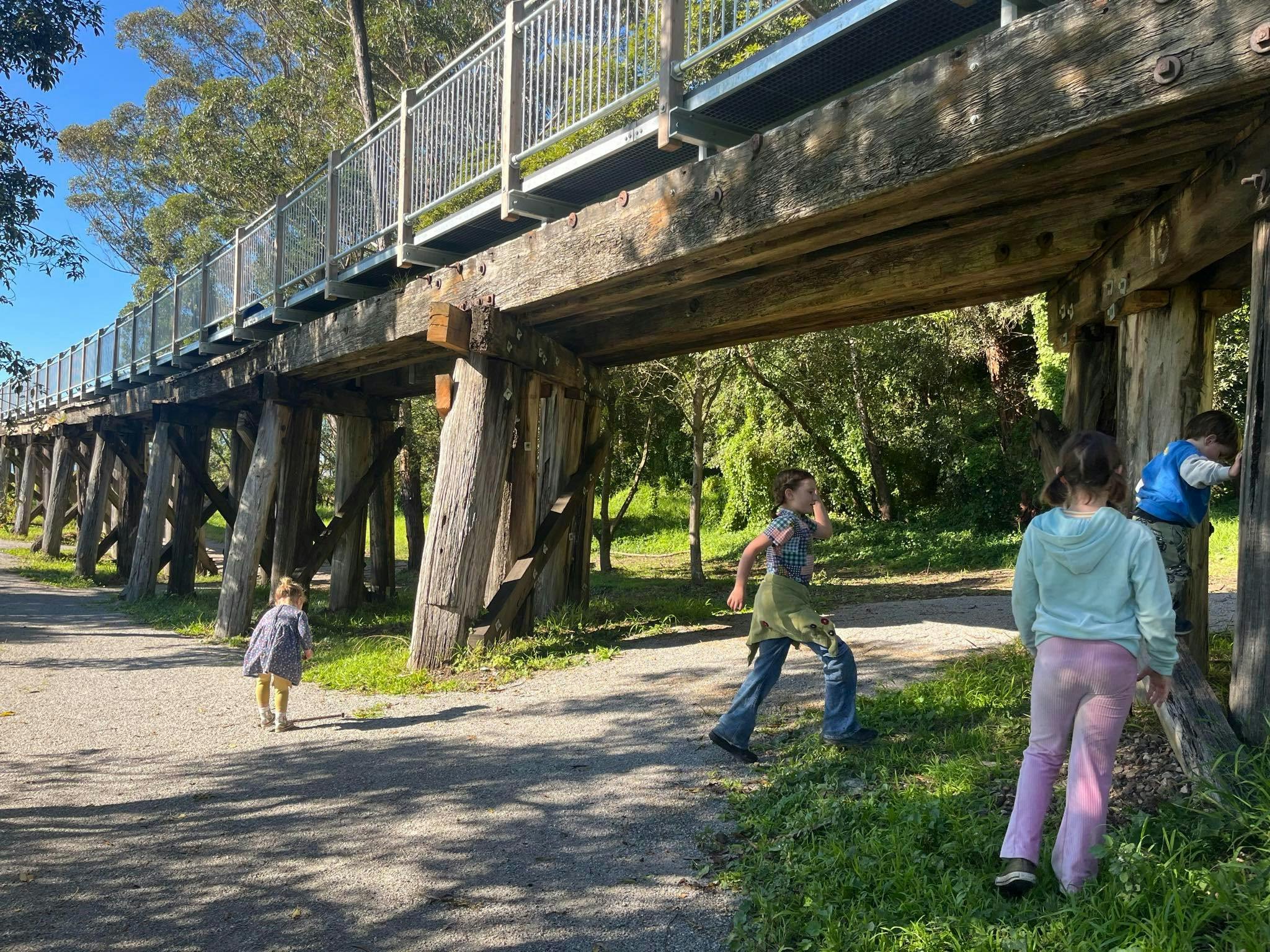 People walking on a trail underneath a timber rail bridge with walking trail above