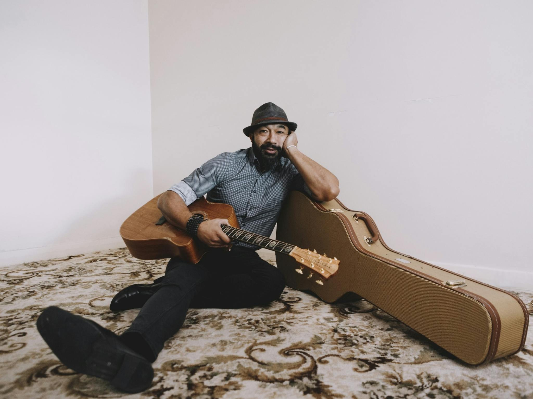 Joe Amputch sitting on the floor with his guitar leaning on the guitar case