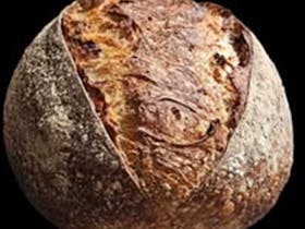 A beautiful crunchy, brown round loaf of handmade sour dough bread.