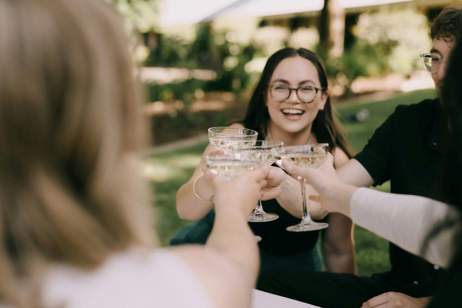 smiling friends holding up cocktail glasses together doing cheers