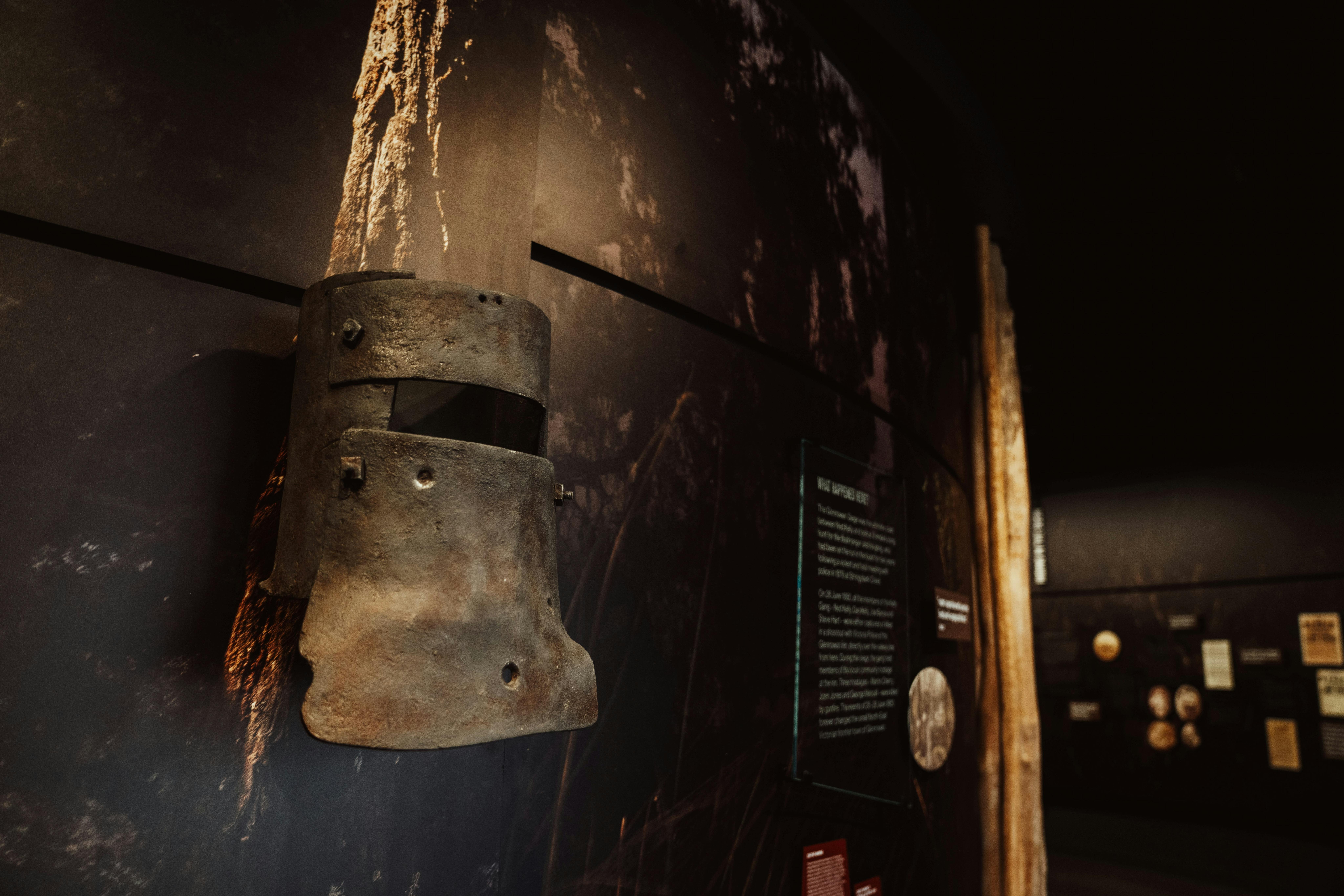Replica of Ned Kellys iron helmet  on the wall with a dark bush scene.