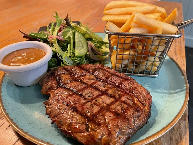 A close up image of a plate of food - steak, fries, a green salad and a small ramekin on sauce