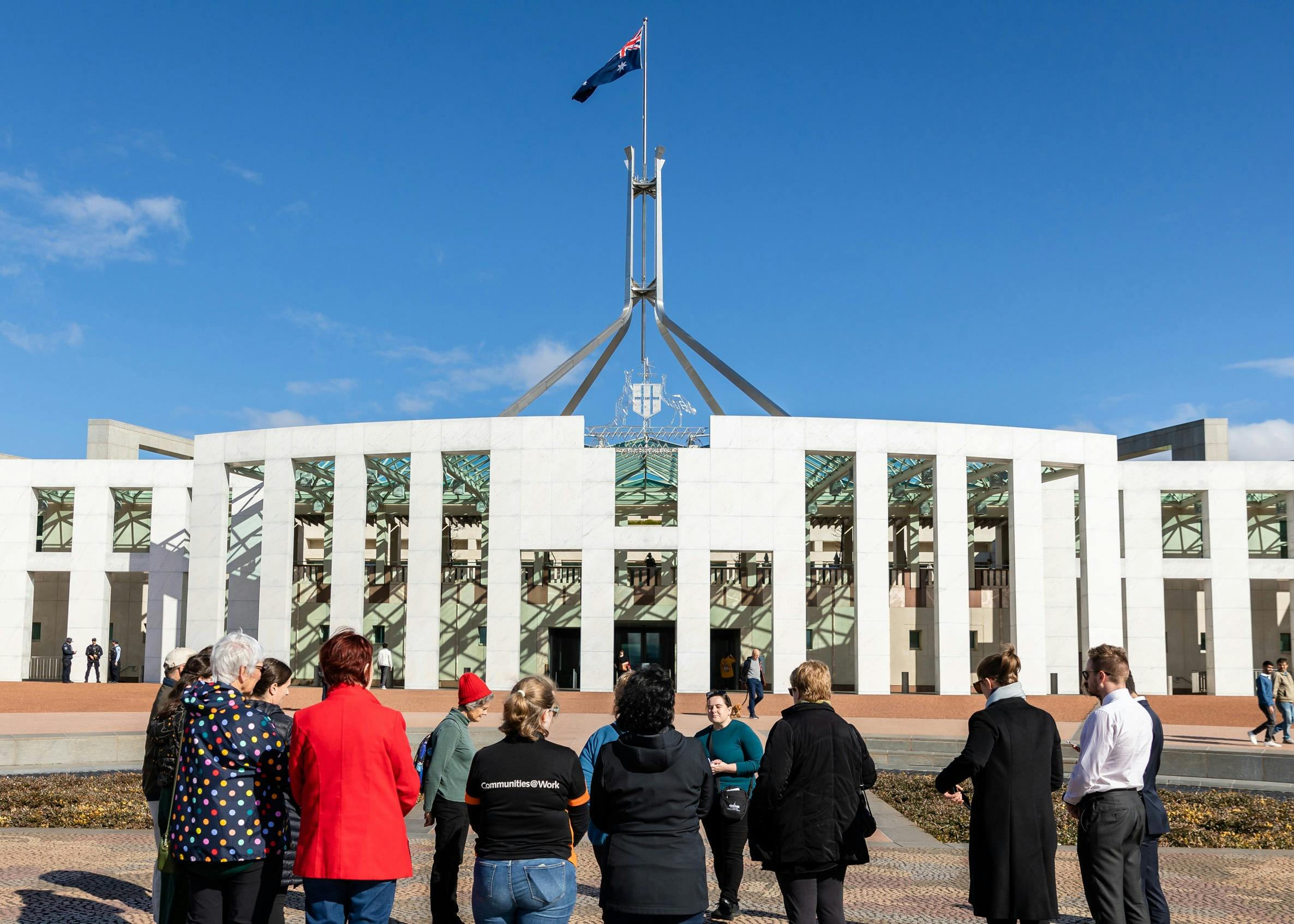 Tour group stands outside Parliament House on the Forecourt Mosaic listening to a tour guide