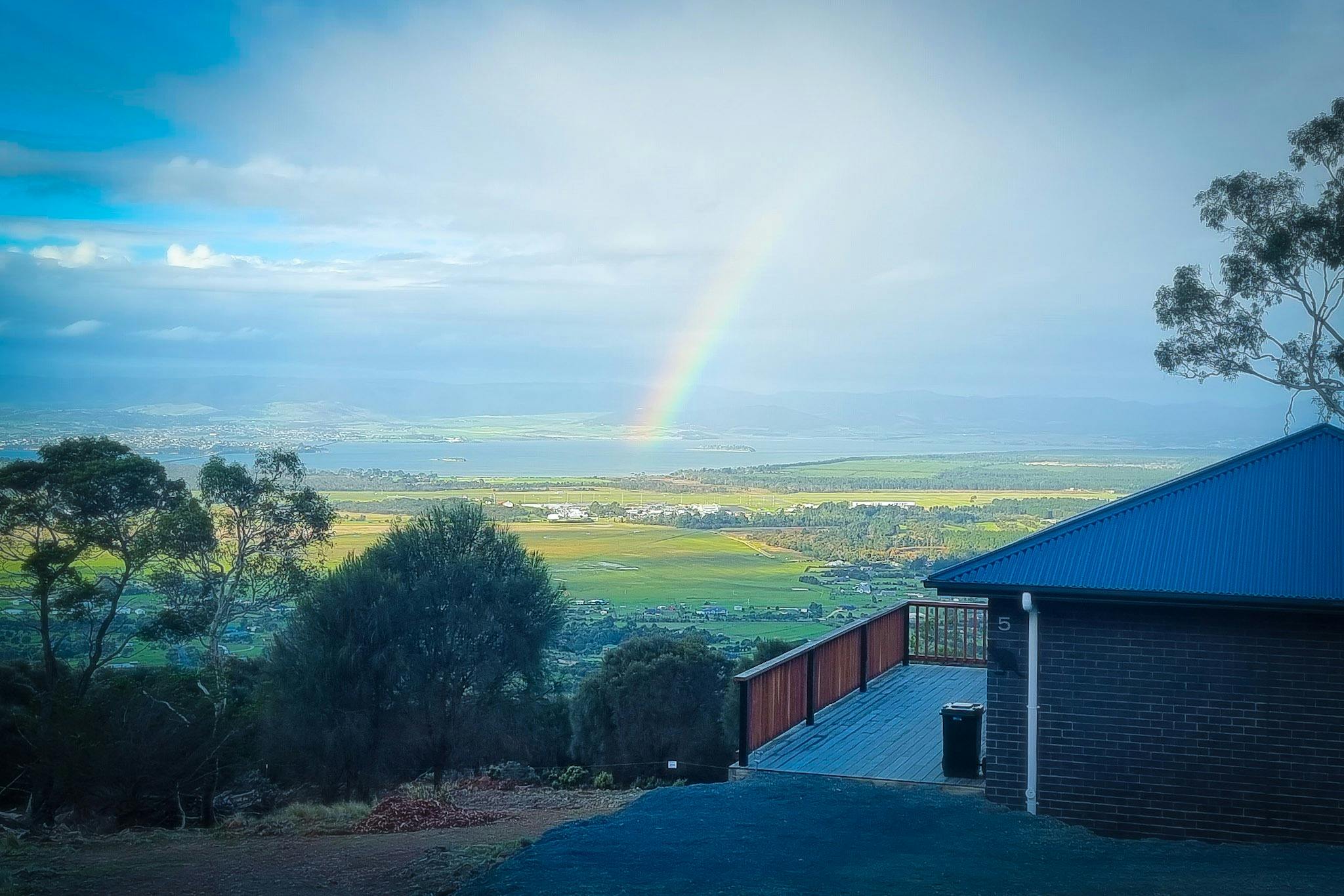 Rainbow stretching across the rural Tasmanian landscape viewed from Mt Rumney