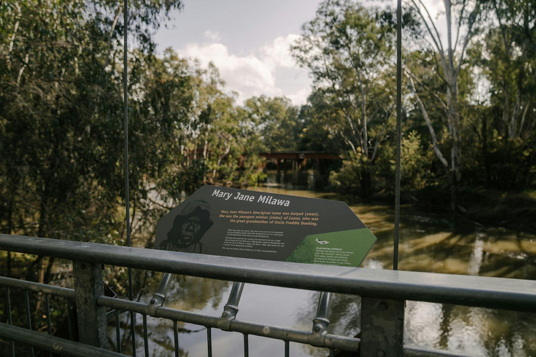 Grey sign with cultural information on the side of a swing bridge.