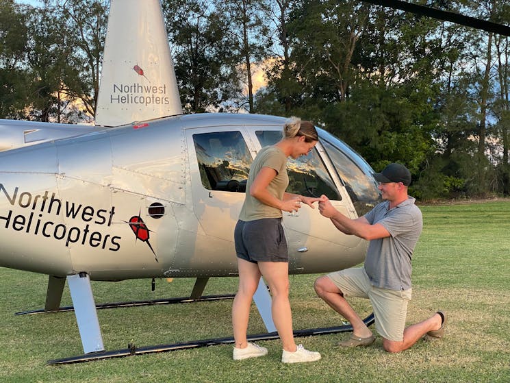 A man kneeling and proposing with a ring, to his soon to be fiance, in front of the Helicopter