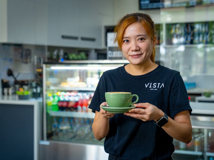 staff member holding a cup of coffee in a green cup