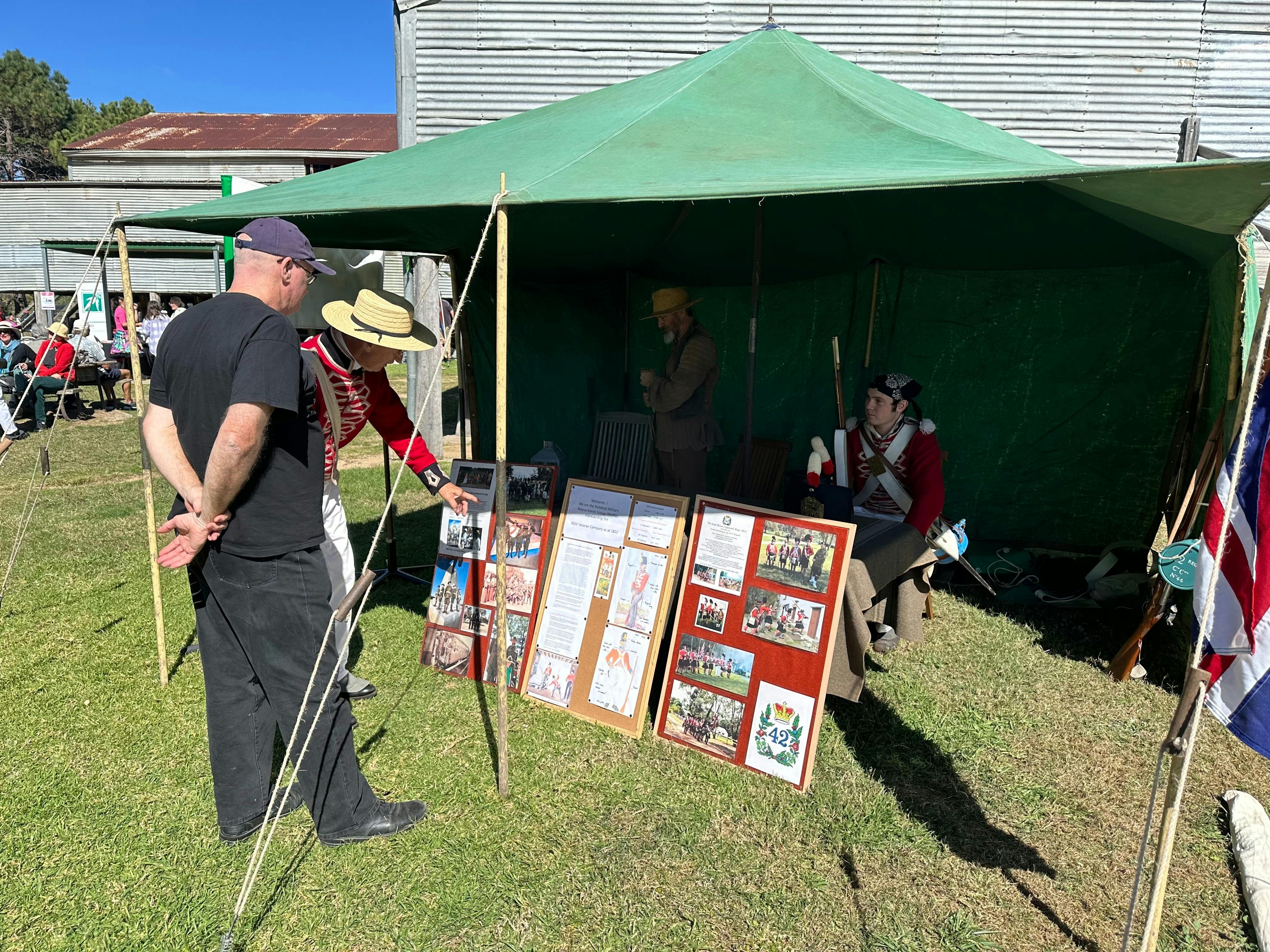 Man outdoors looking at photographic display at a marque with m another man dressed as a soldier