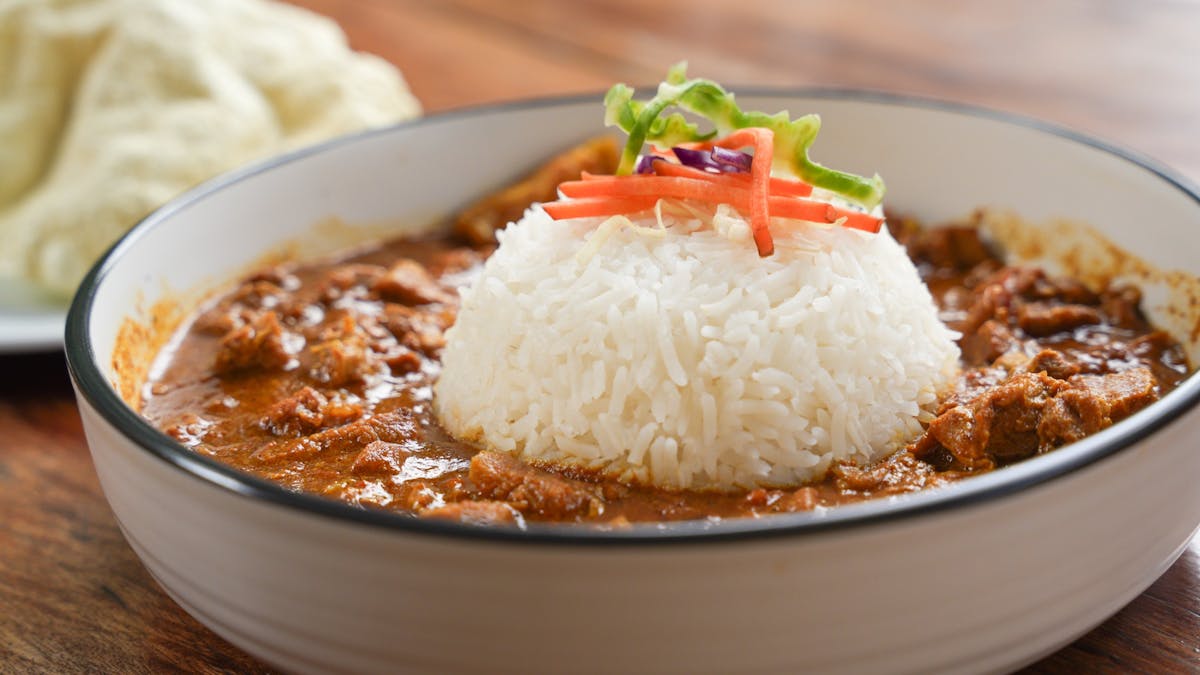 Plate with rice and butter chicken on table, beer and singer in background