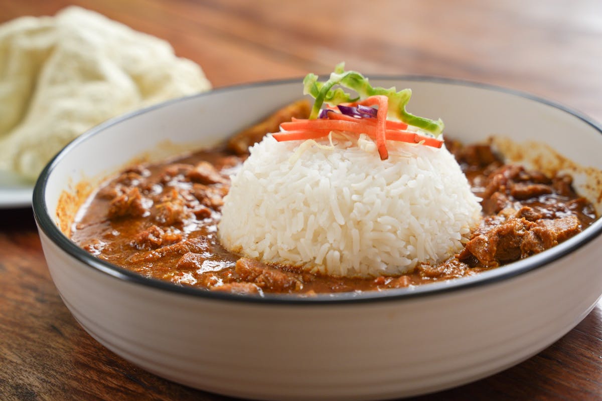 Plate with rice and butter chicken on table, beer and singer in background