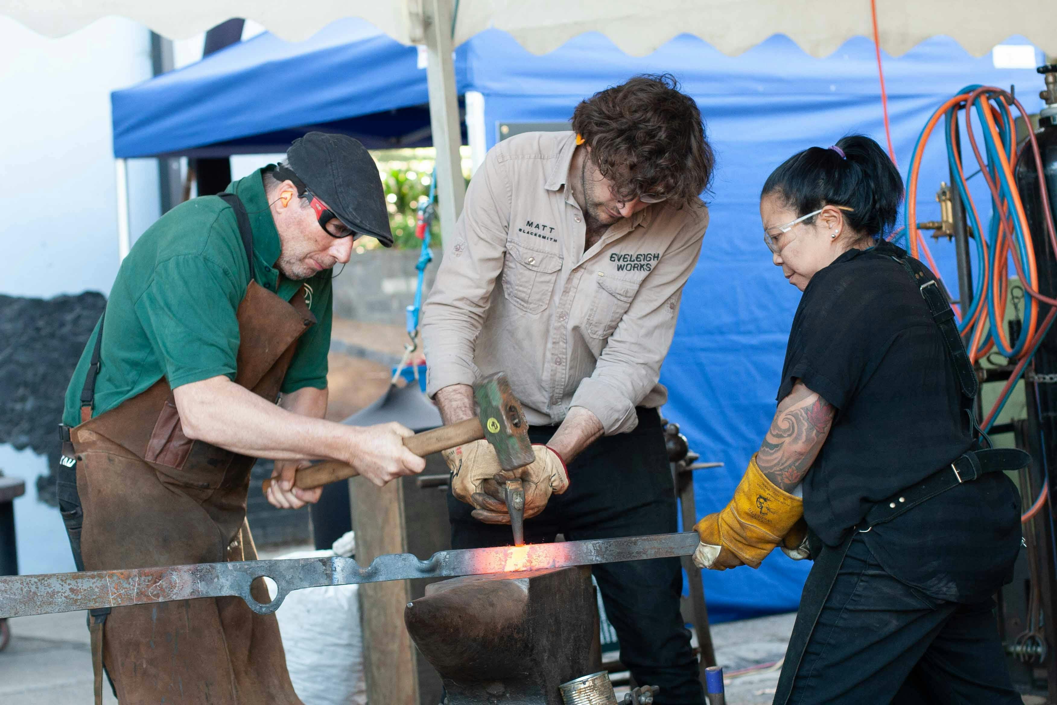 A team of blacksmiths works together, forging hot iron for a collaborative sculpture project